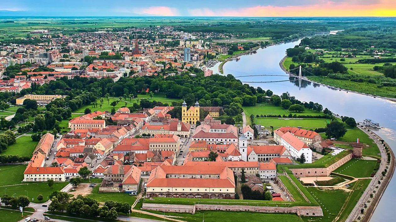 Aerial view of a historic fortress with red rooftops beside a winding river at sunset.