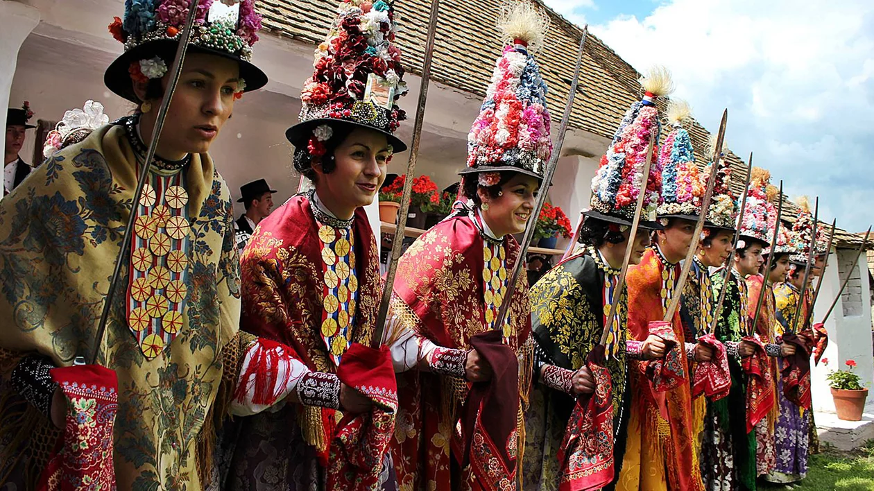 People in vibrant traditional costumes and elaborate hats standing in a row outdoors.