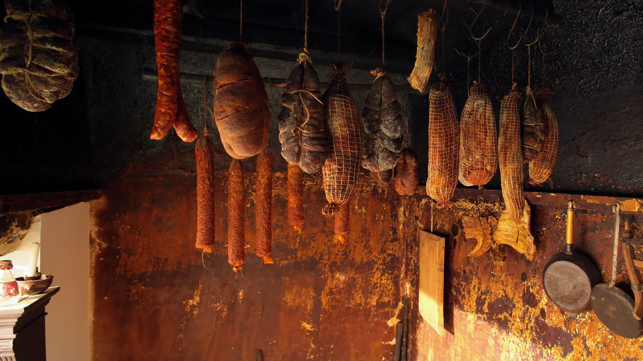 Various cured meats and sausages hanging from the ceiling in a rustic smokehouse.