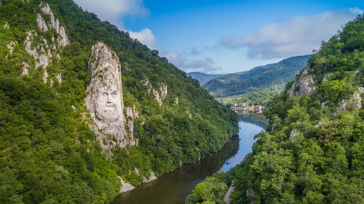 River winding between green forested hills under a blue sky with scattered clouds.