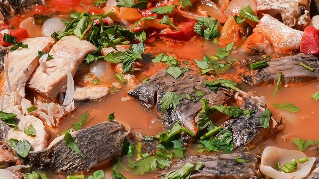 Fish stew with chunks of fish, tomatoes, herbs, and vegetables in a red broth.