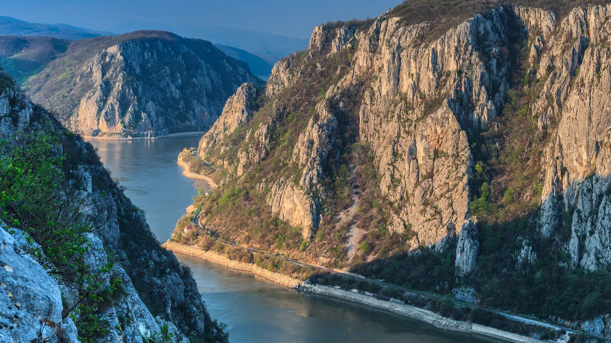 Steep rocky cliffs and a winding river in a sunlit mountain gorge.