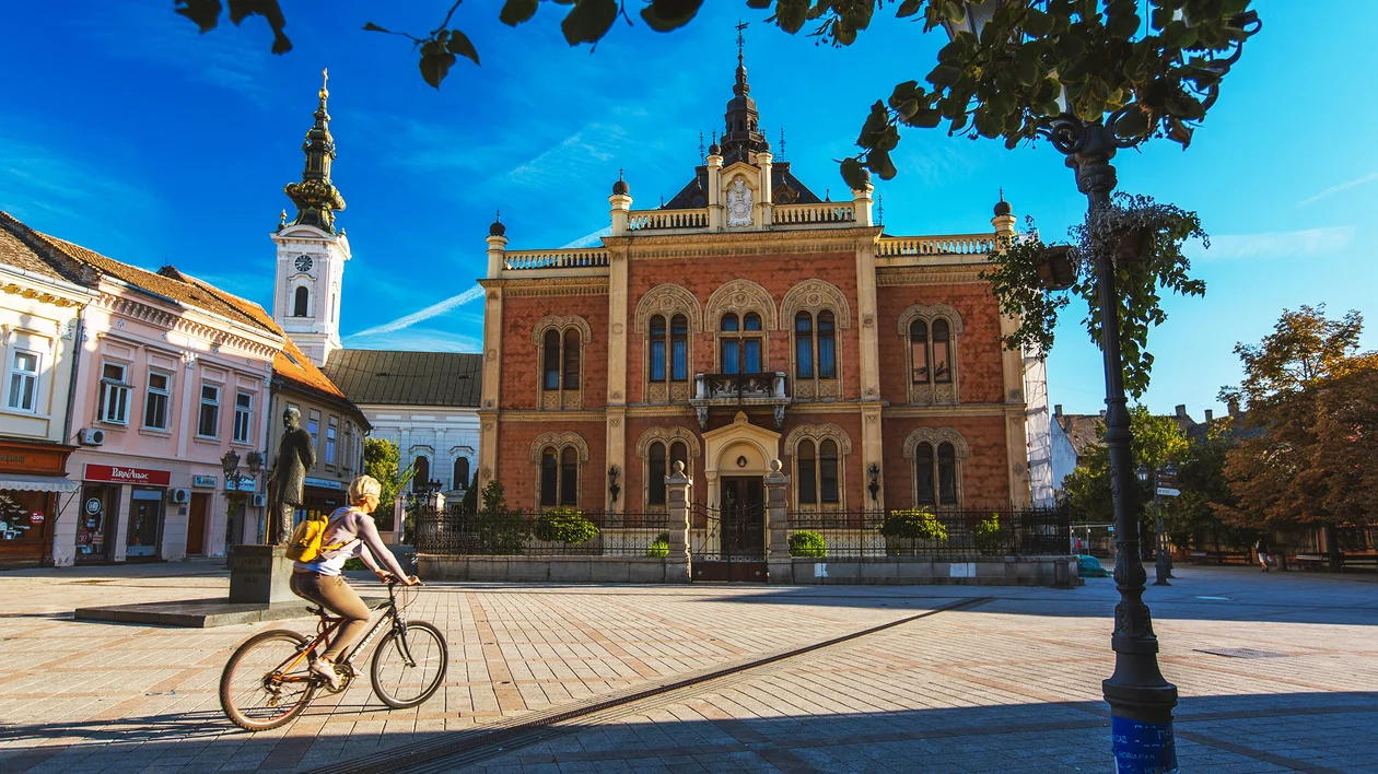 Person riding a bike past a historic building under a clear blue sky.