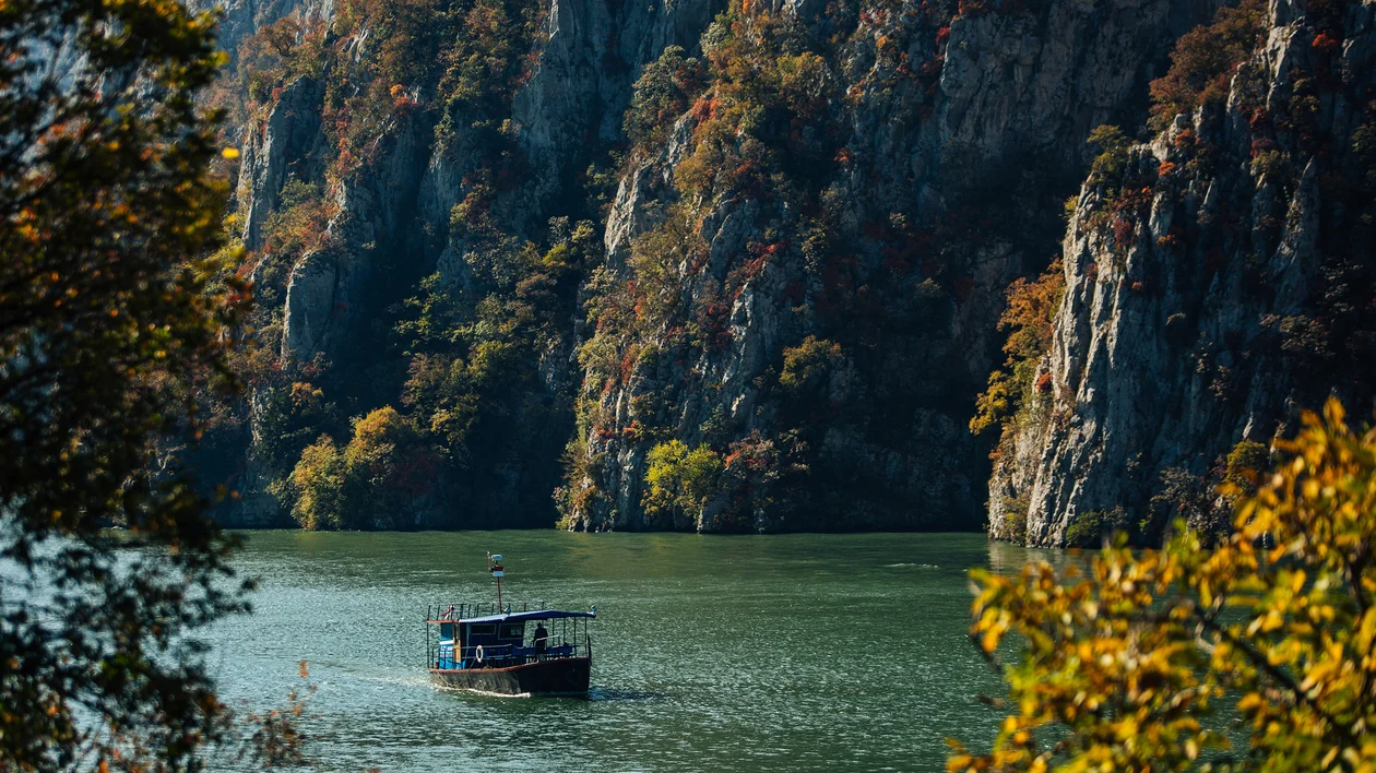 Boat on a calm river surrounded by cliffs and autumn trees.