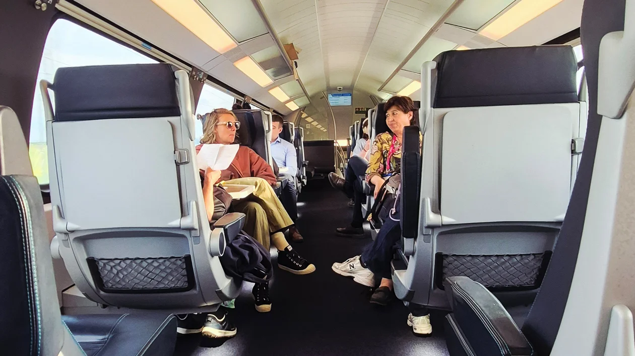 Passengers sitting inside a modern train carriage, some reading or talking.