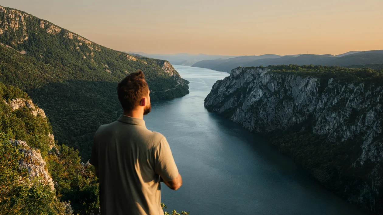 Man overlooking a river canyon at sunset, surrounded by green cliffs.