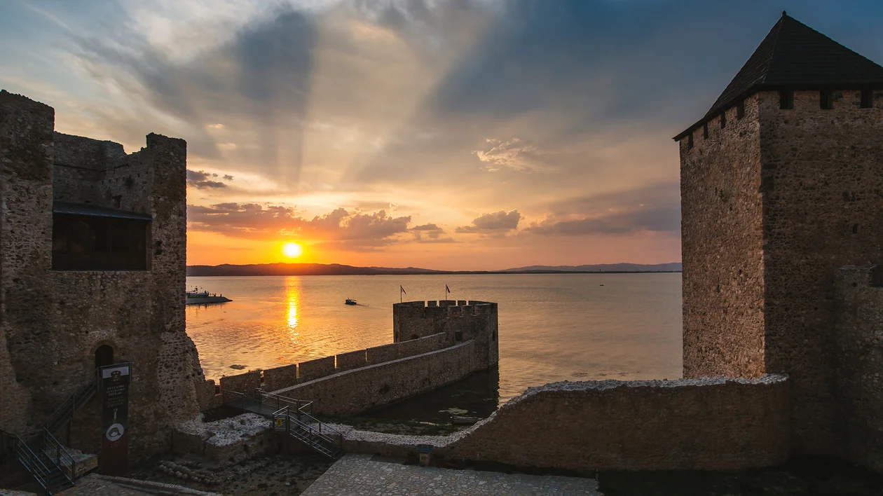 Medieval fortress by a lake with a dramatic sunset and rays breaking through clouds