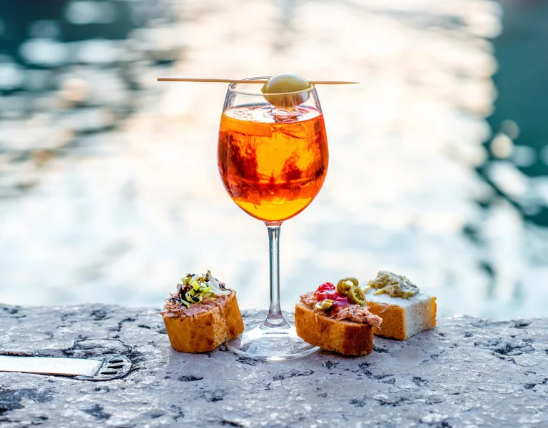 Spritz Aperol drink with venetian traditional snacks cicchetti on the water chanal background in Venice