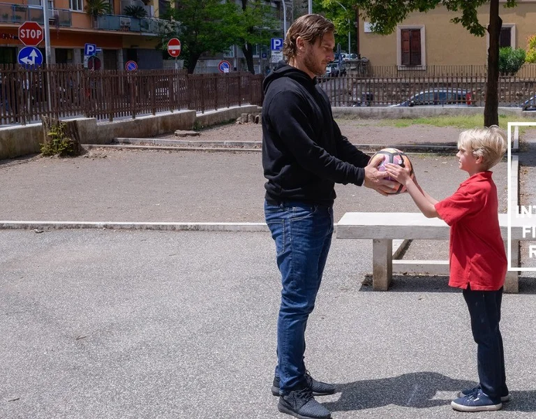 Man and boy facing each other in a park, holding a soccer ball between them.
