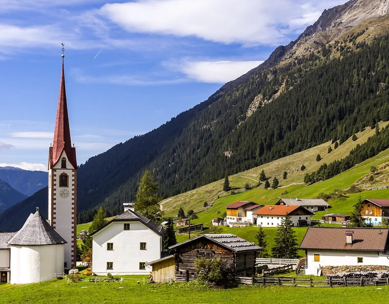 Small village with a church steeple, green hills, and mountains in the background.