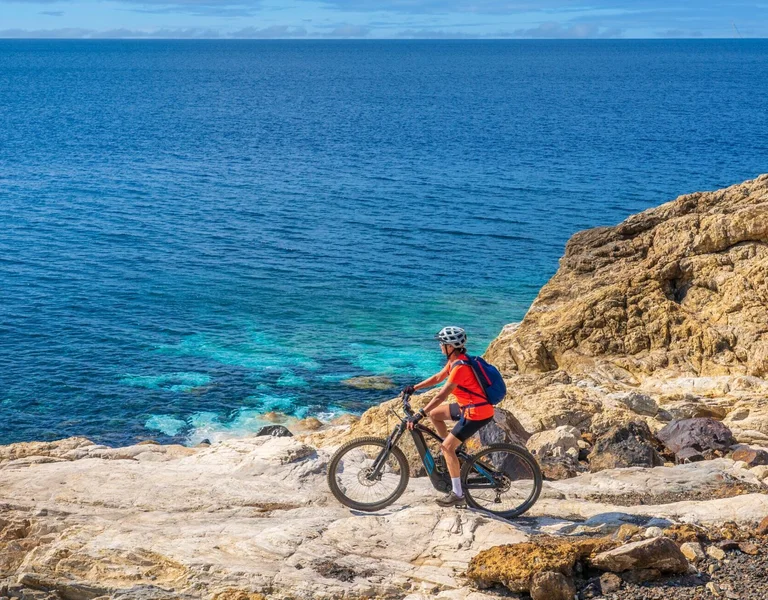 Cyclist in a red shirt riding on rocky cliffs by the blue sea.