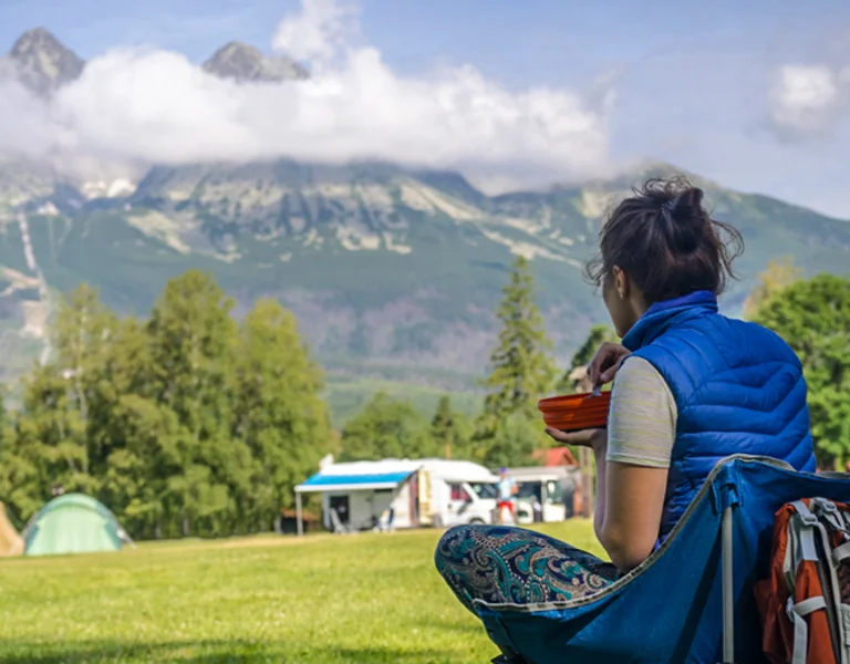 A woman is eating her lunch in front of a stunning mountain landscape.