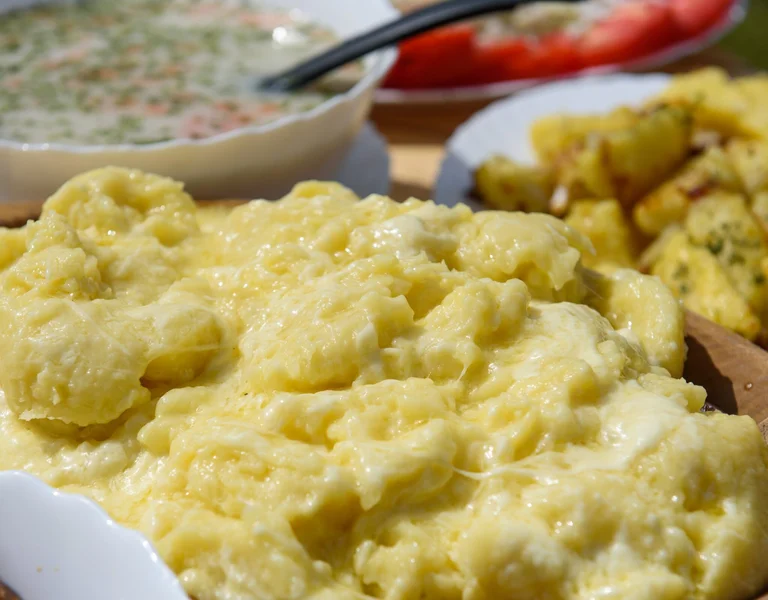 Kacamak is a typical Montenegrin plait made with eggs and polenta, served on a wooden ball with soup and potatoes in the background.