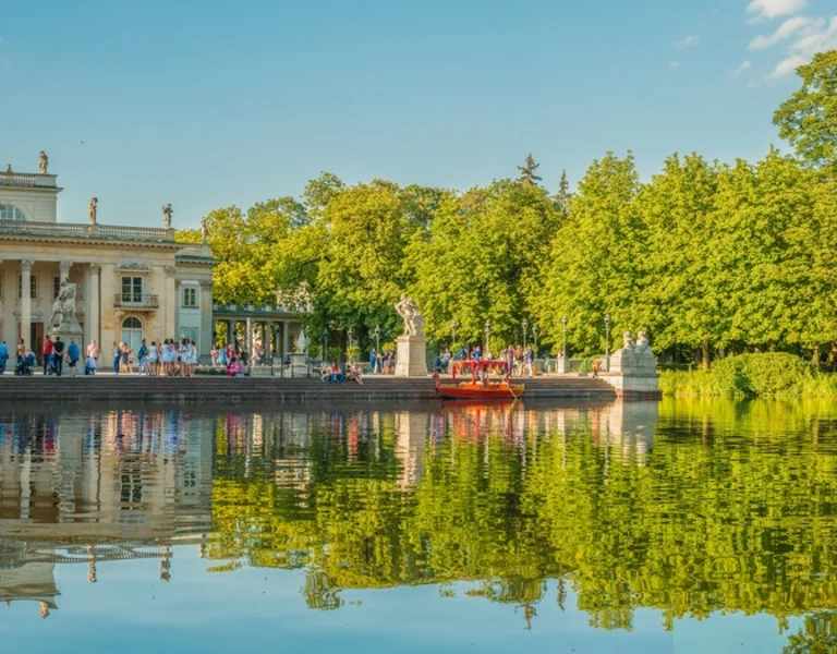 Panoramic view of a historic palace by a lake with people in boats and greenery around.