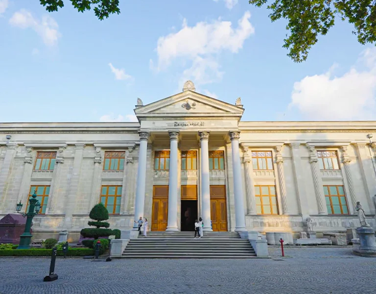 Classical building with columns and steps, adorned with sculptures and surrounded by greenery.
