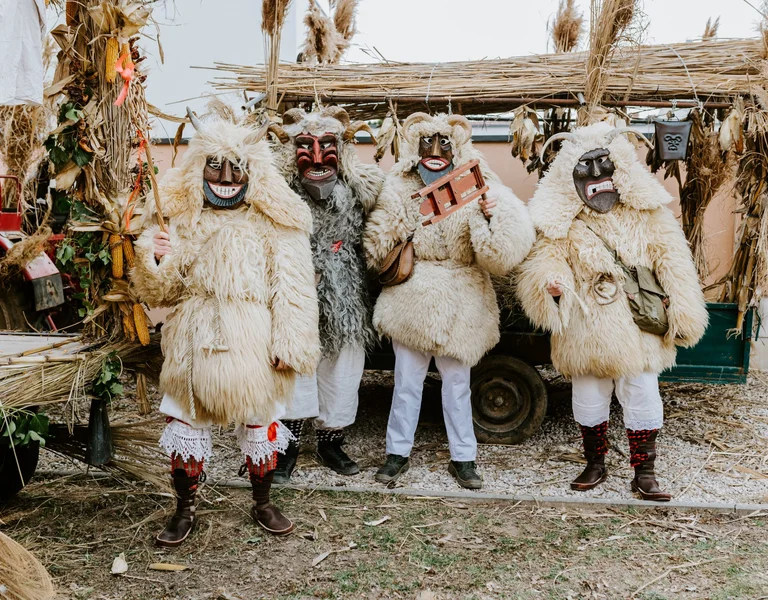 People in traditional furry costumes with masks standing in front of a straw hut.