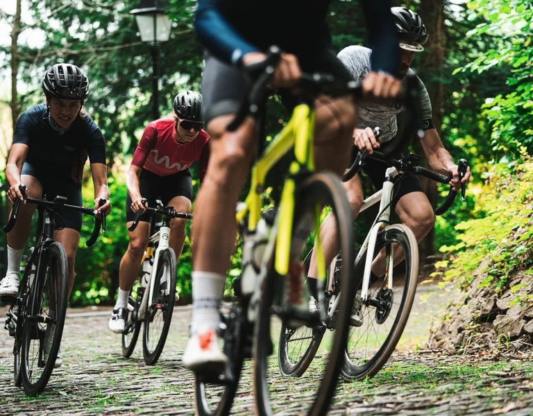 Group of cyclists riding on a cobblestone path surrounded by greenery.