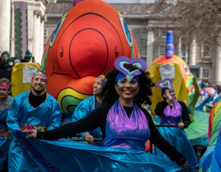 St Patrick's Festival parade with vibrant inflatable costumes and participants in blue raincoats.