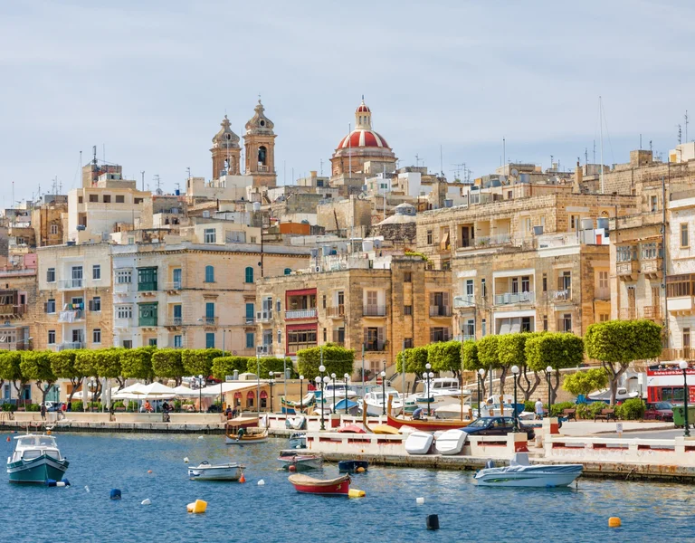 La Valletta harbor with boats and historic buildings with domes in the background.