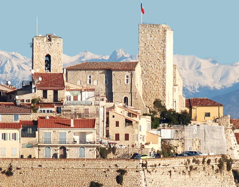The historic fortified town of Antibes on the French Riviera, framed by the clear blue Mediterranean and snow-capped Alps in the background.