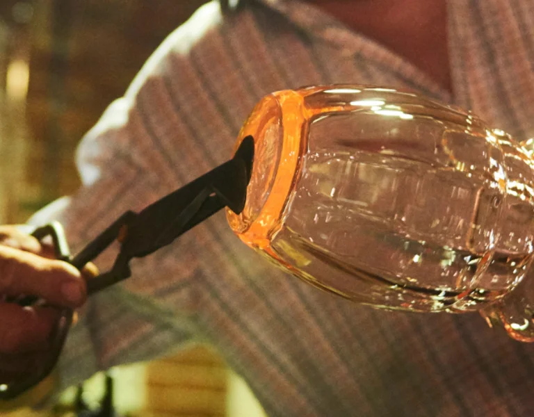 A skilled artisan crafting a glass vessel in a traditional glassmaking workshop, surrounded by warm, rustic ambiance.