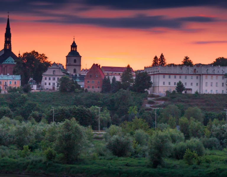 A picturesque town skyline at sunset, featuring historic buildings and a church steeple against a vibrant orange and purple sky.