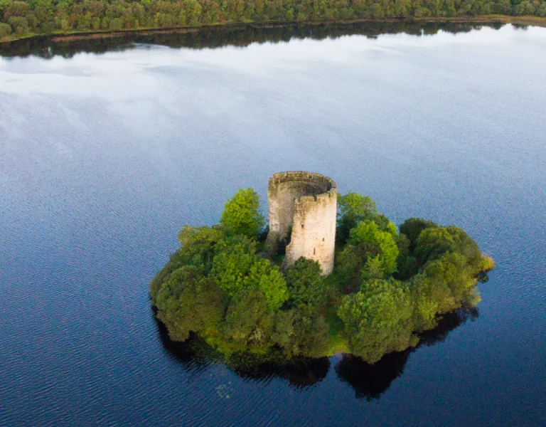 A small forested island with a stone tower in the middle of a lake in Ireland.