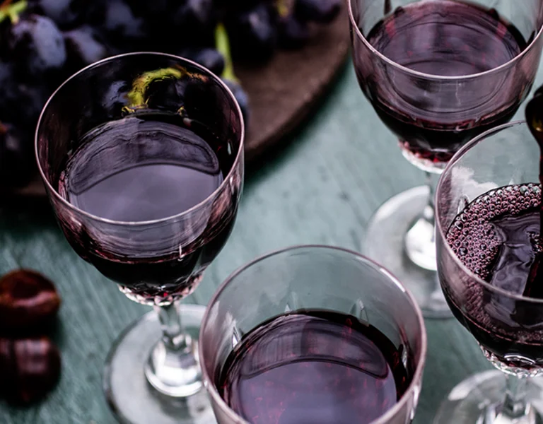 Red wine being poured into glasses on a rustic outdoor table with grapes and chestnuts