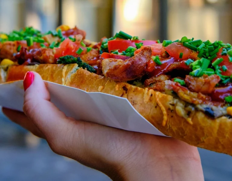 Traditional Polish zapiekanka, an open-faced baguette with melted cheese and toppings, held in hand.