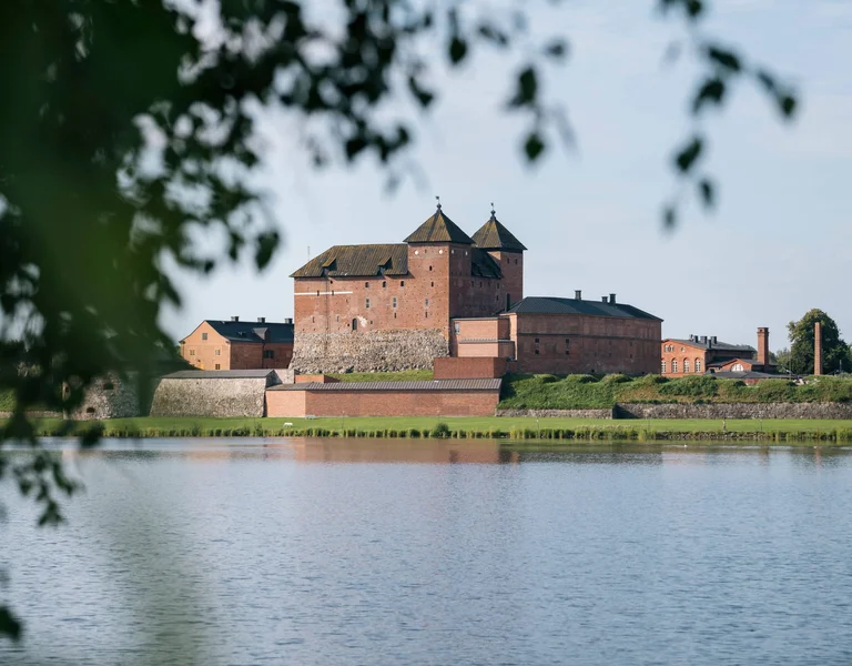 Medieval Hamelina Castle on a cloudy day, situated along a river, with trees lining the riverbank in the foreground.