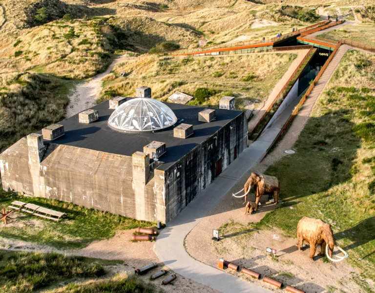 Tirpitz Museum in Denmark seen from a bird's-eye view, surrounded by open fields with mammoth sculptures