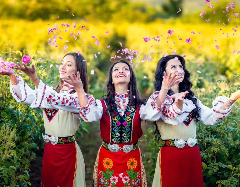 People celebrating at the Rose Festival in Kazanlak, Bulgaria, surrounded by blooming roses and colorful traditional costumes.
