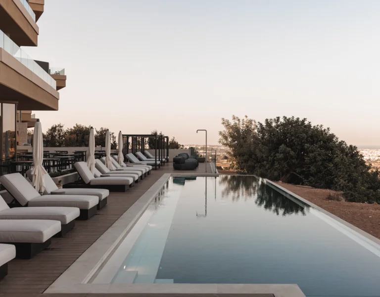 Modern infinity pool with white sun loungers on a wooden deck overlooking a look in malta from Verdala Wellness Hotel