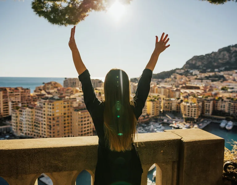 Woman with the two arms open in Monaco with a blue sky and the city around.