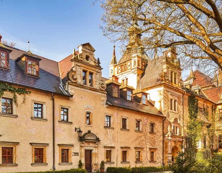  Kliczków Castle in Poland with historic façades, ivy-covered walls, and towers in warm evening light
