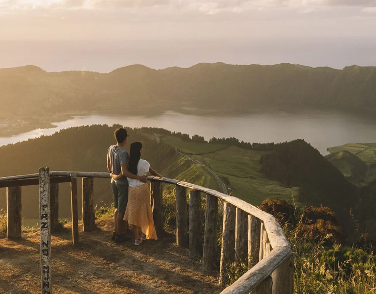 Couple overlooking twin crater lakes from a wooden viewpoint at sunset.