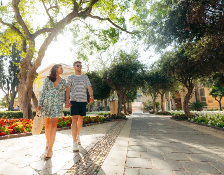 Couple walking hand in hand along a tree-lined Mediterranean promenade