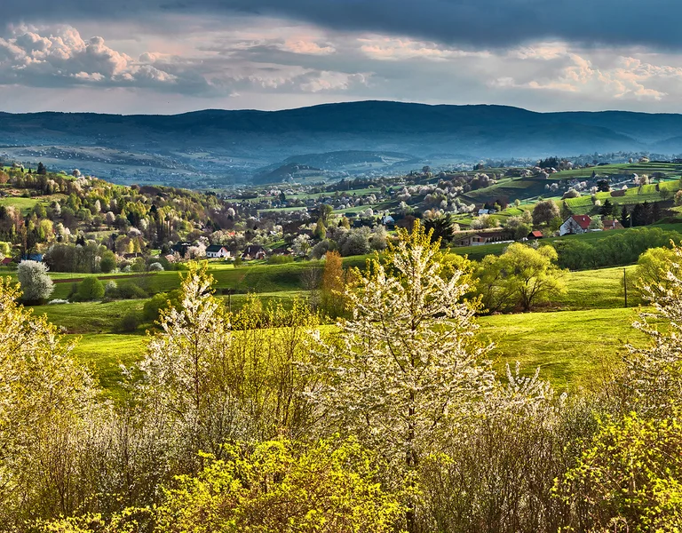 Rolling green hills with scattered houses under a dramatic cloudy sky.