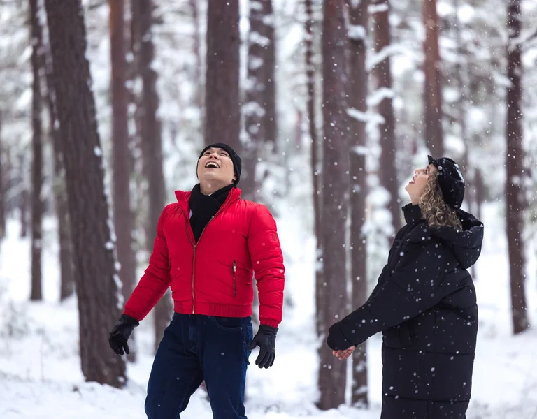 Couple enjoying snowfall during a winter walk in a snowy forest