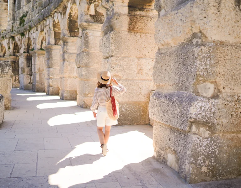 Woman in a hat walking along ancient stone ruins in sunlight.