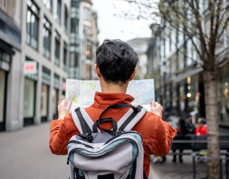 Person with a backpack looking at a map on a city street.