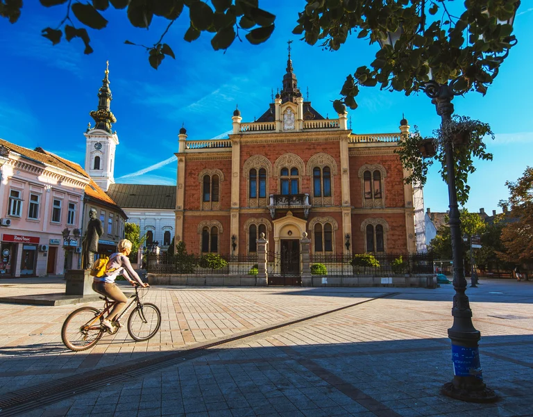 Cyclist riding through a sunny town square with historic buildings and a church.