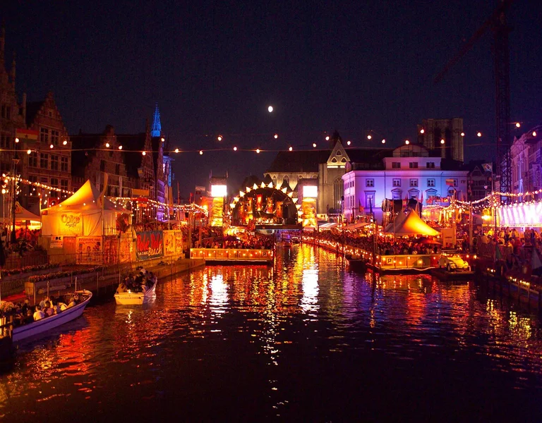 Festive canal scene at night with colorful lights and boats, buildings in the background.