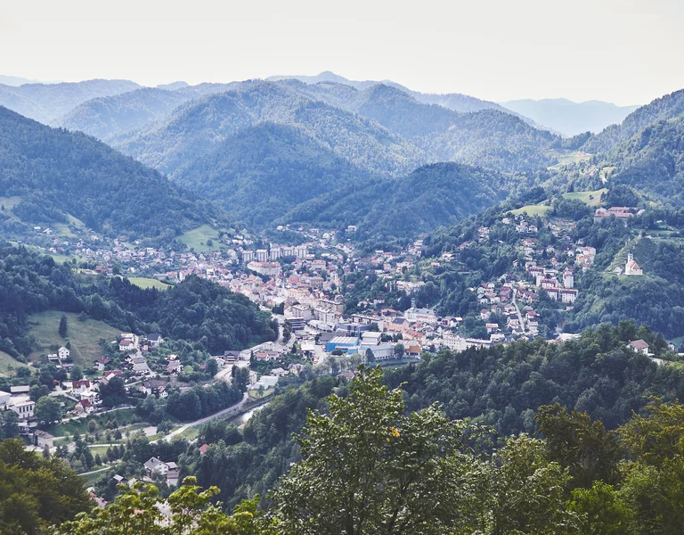 Town nestled in a lush green valley surrounded by forested mountains.