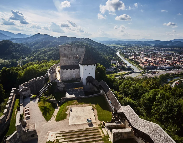 Hilltop castle overlooking a city with mountains in the background on a sunny day.