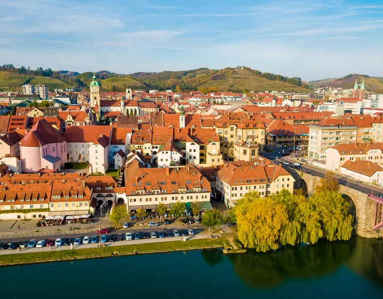 Red-roofed town by a river, green hills in the background, sunny day.
