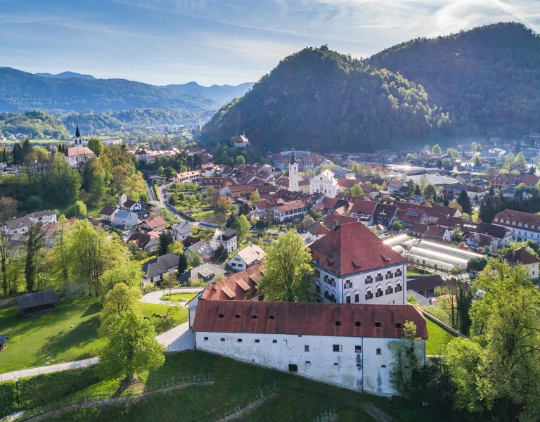 Aerial view of a town with red-roofed buildings surrounded by green hills and mountains.