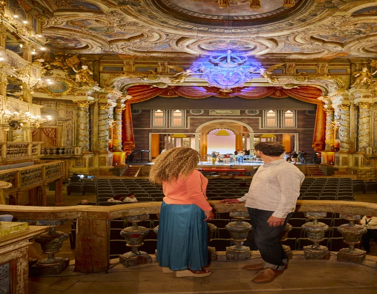 Two people admire an ornate, brightly lit theater from a balcony.