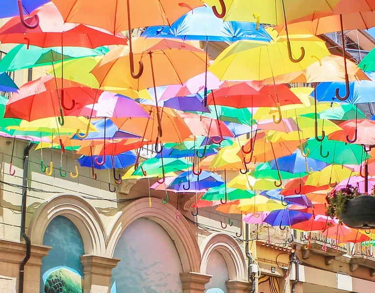 Brightly colored umbrellas suspended above a sunny street with arches and a lamp post.
