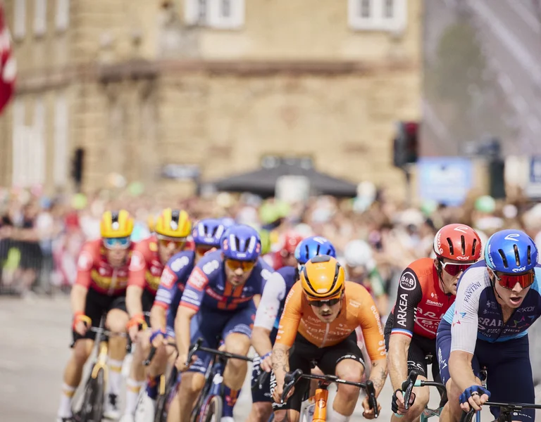 Cyclists racing through a city street with spectators and Danish flags in the background.